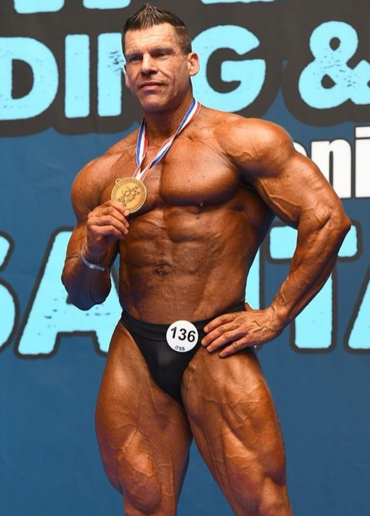 En bild på tränaren som ler medan hen håller i en medalj.